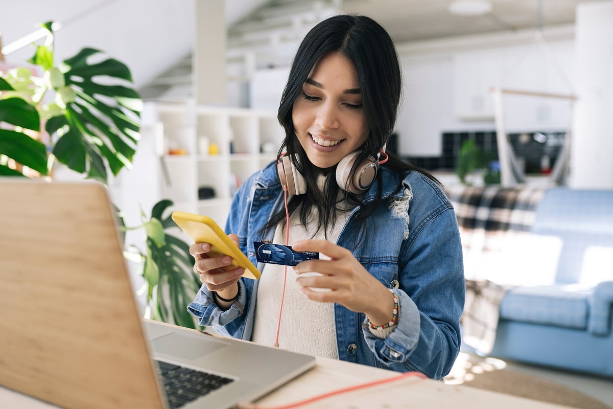 A stylish, high-quality lifestyle photo of a person relaxing in a well-designed living room, shopping online with a sleek laptop, and confidently holding a premium rewards credit card to make a purchase.
