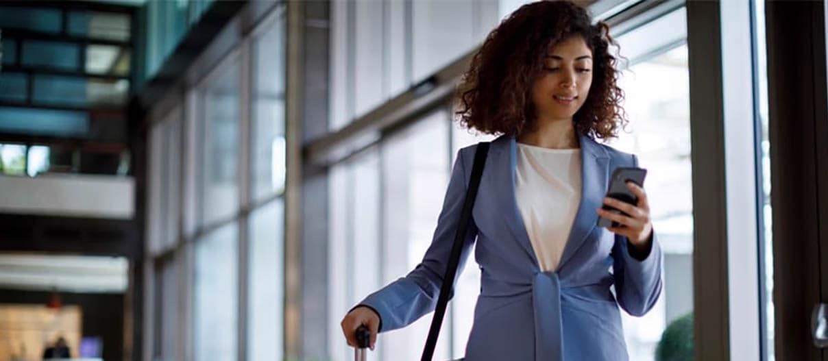 Woman standing with her suitcase looking at her phone