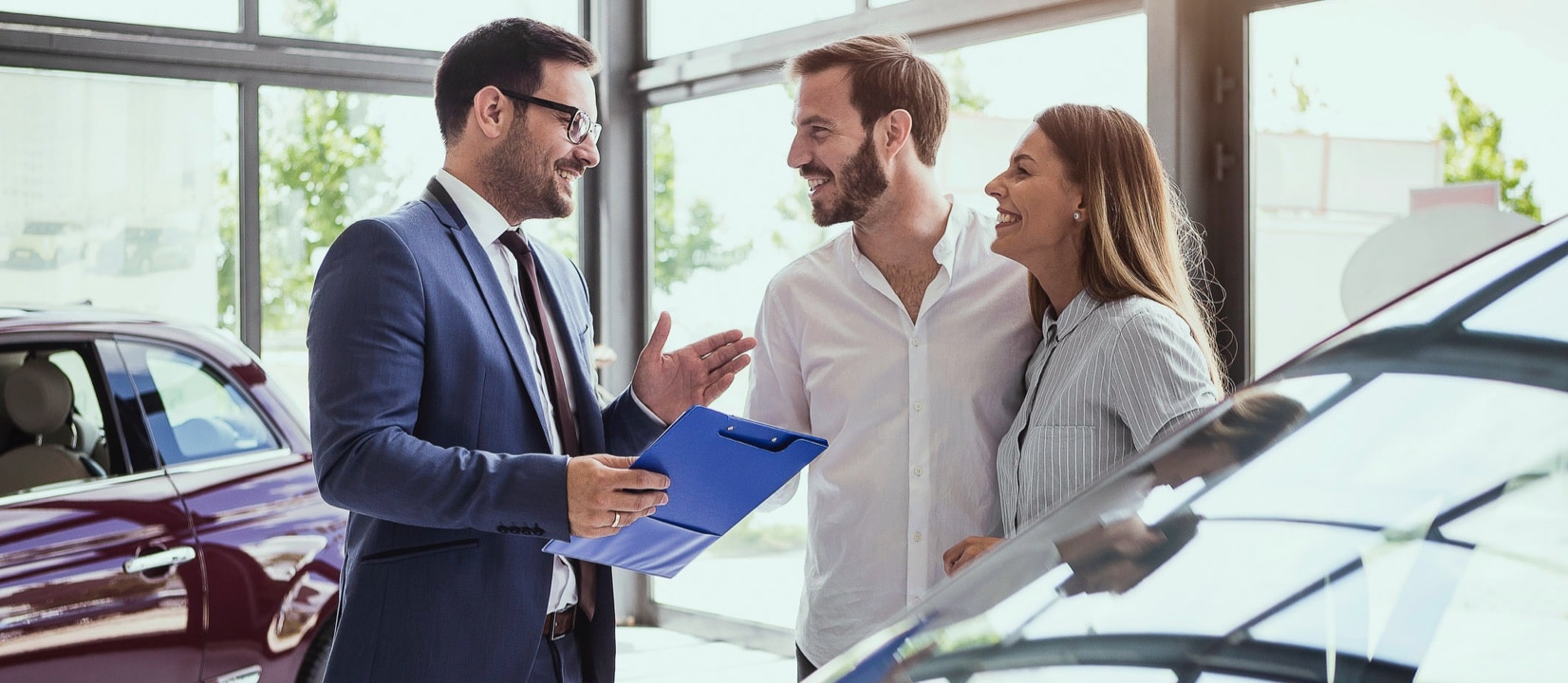 A couple smiling while a car salesman is talking with them