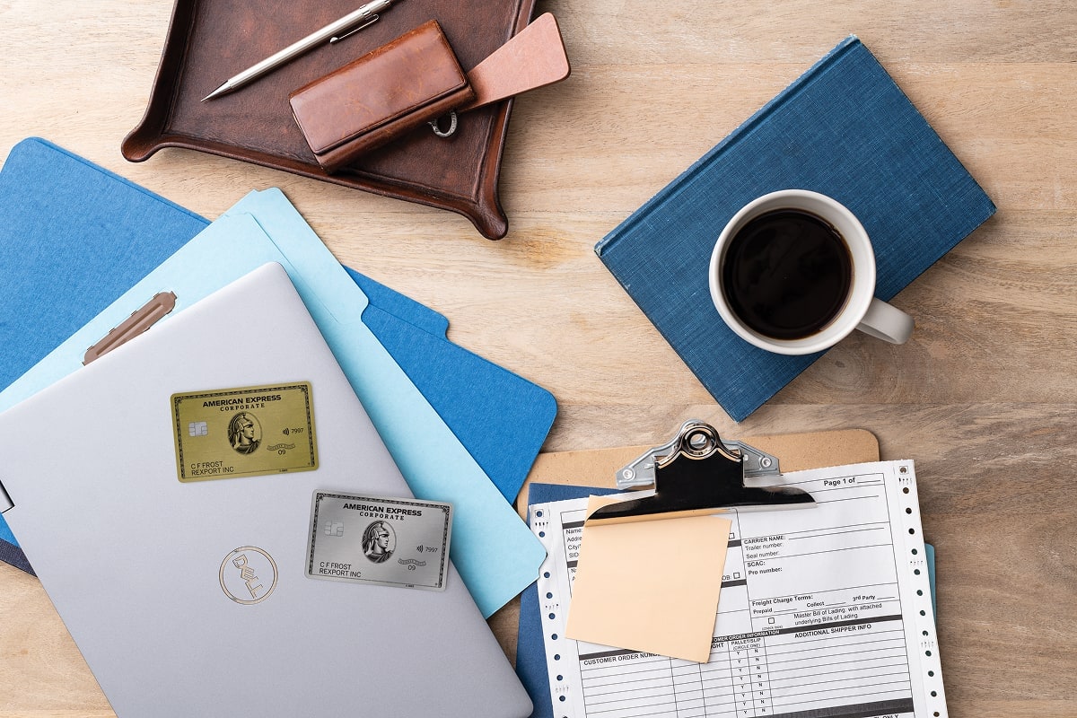 Two amex cards on a laptop on a wooden office desk next to a cup of coffee and paperwork.