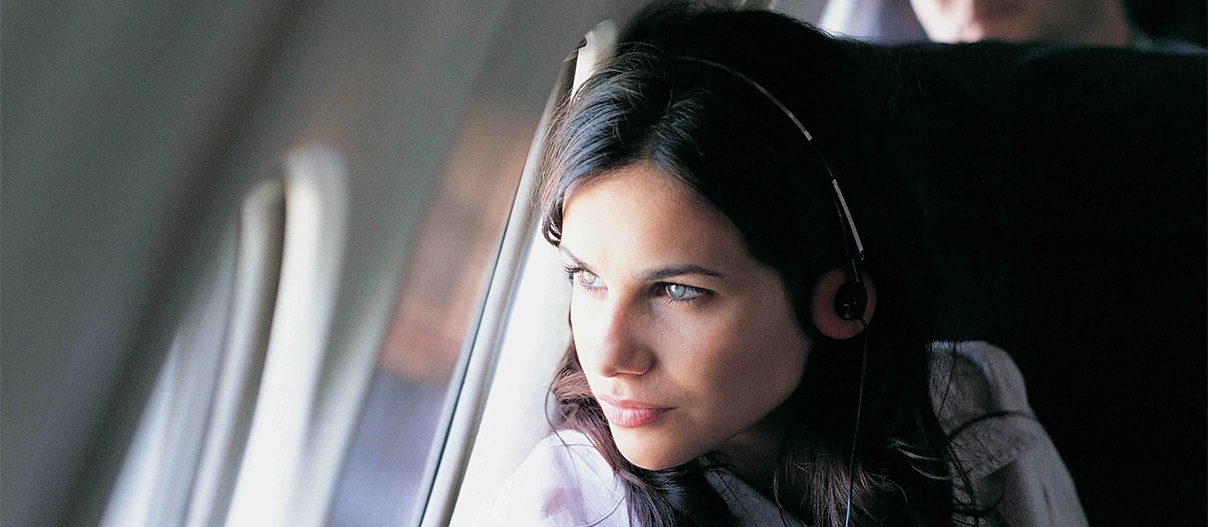 A woman wearing headphones sits comfortably in an airplane, ready to enjoy her journey with cash back or travel rewards.