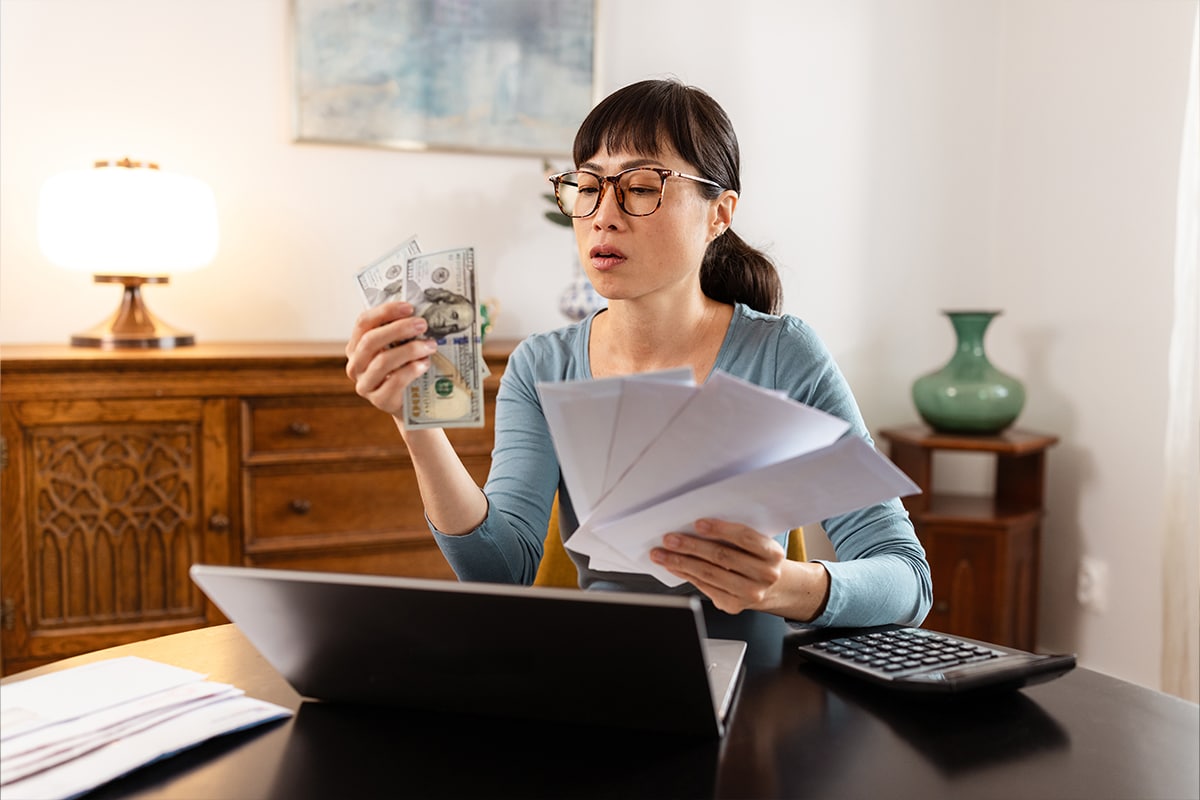 Someone holding some cash or checks and looking contemplative while researching on their phone