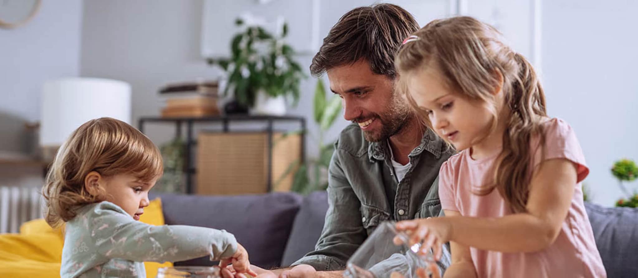 A man and two children play together at a table in a bright living room.