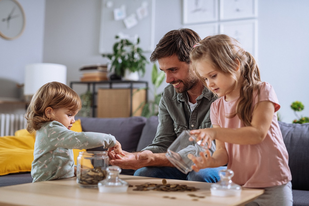 A man and two children play together at a table in a bright living room.
