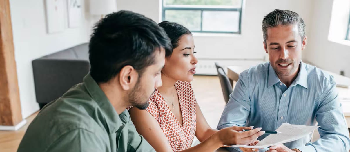 A woman is explaining the potential closing costs on a house to two professional men.