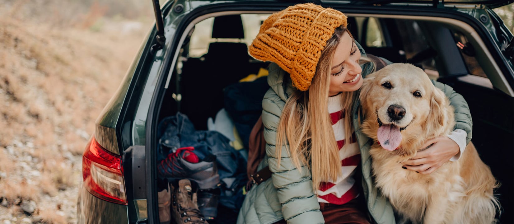 A cheerful woman sitting at the back of a car with a dog.