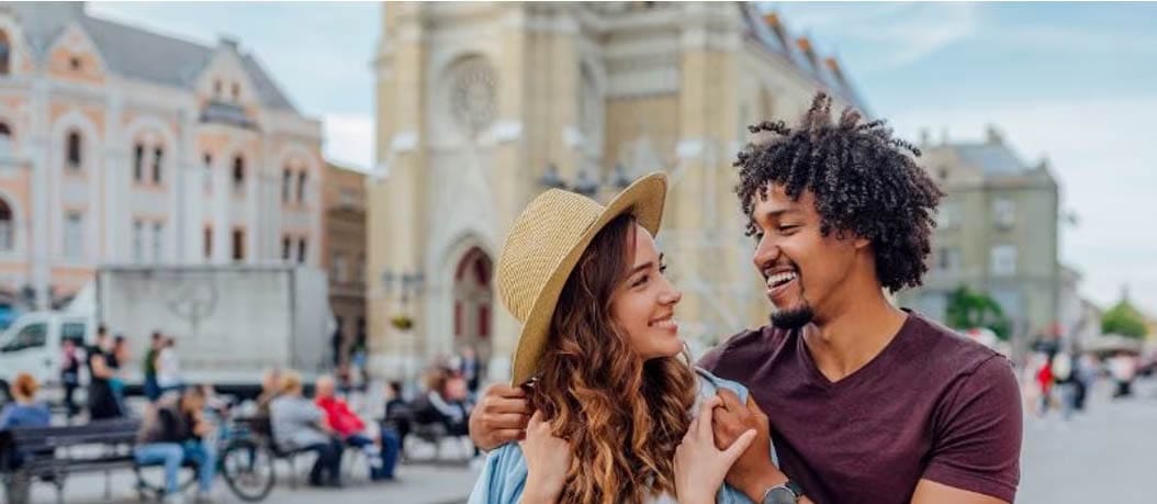 A young couple smiles at each other in the city, embodying joy and connection while exploring travel opportunities together.
