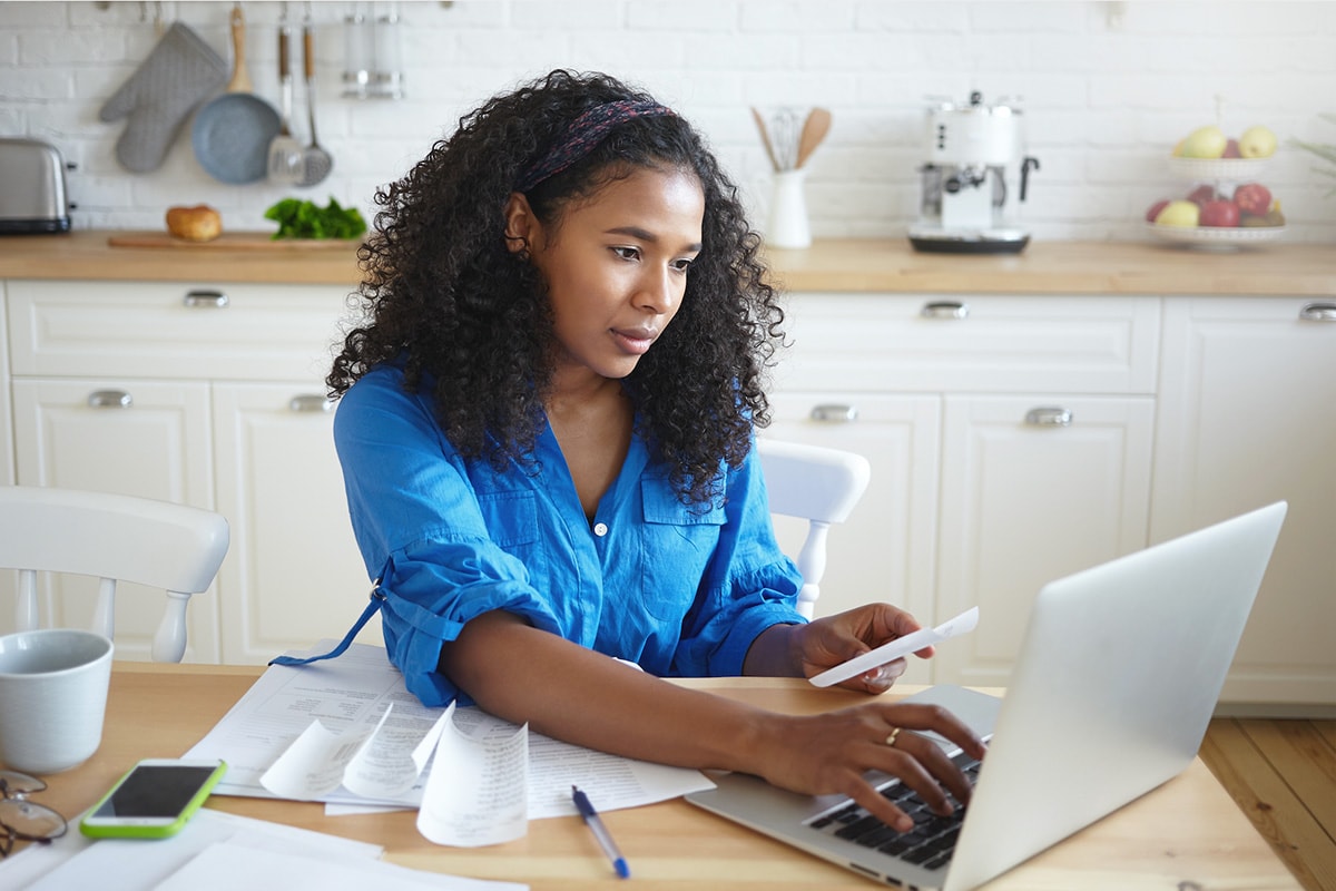A woman seated at a table, focused on her laptop, exploring tips for wisely using credit card benefits.