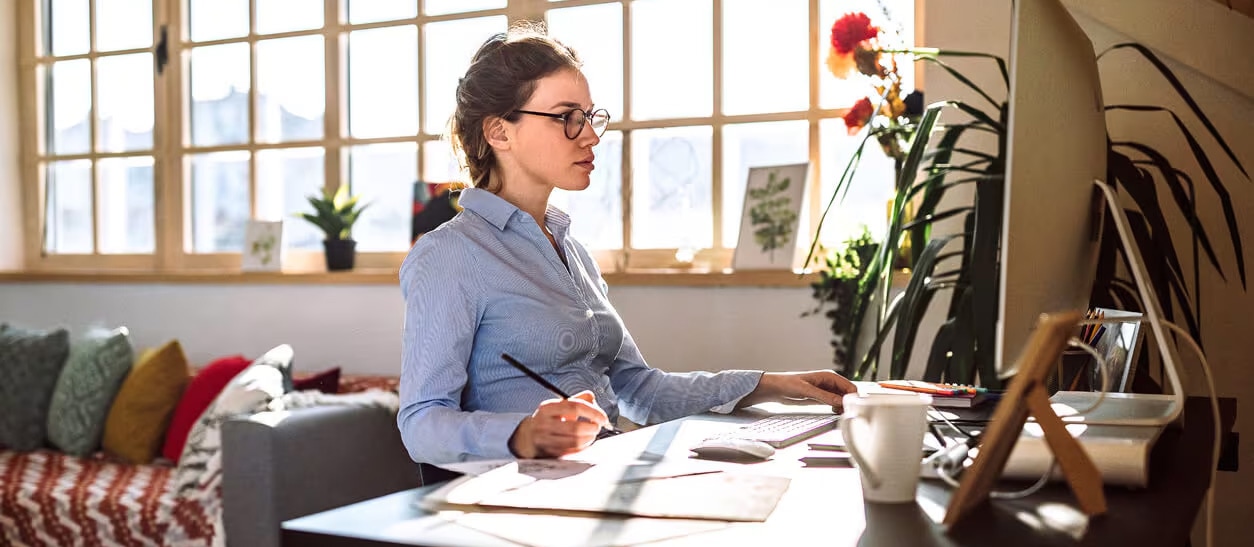 A woman in glasses sits at a desk with a laptop, focused on managing credit card debt after losing her job.