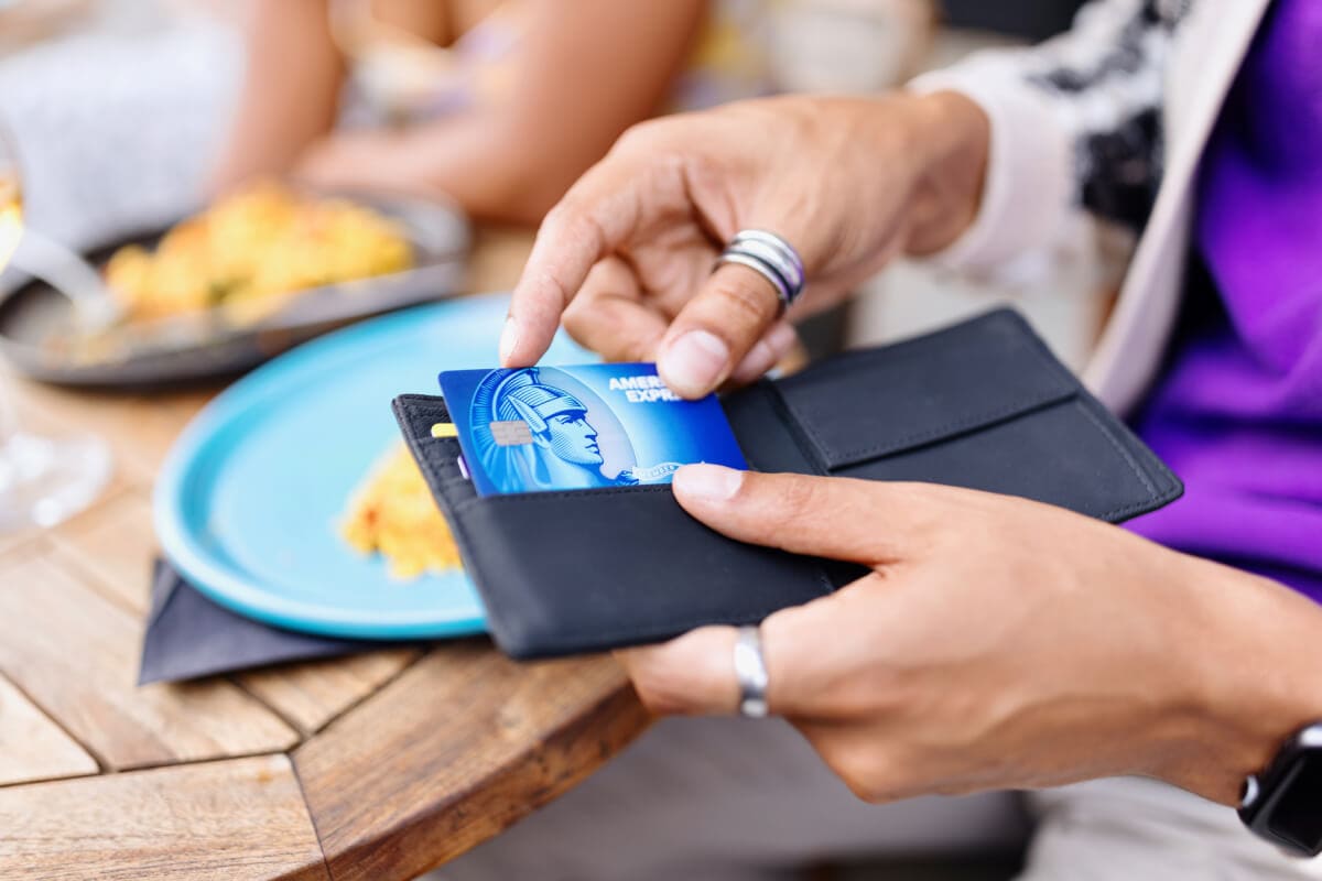A person placing a credit card into a neatly organized wallet with other credit cards and receipts.