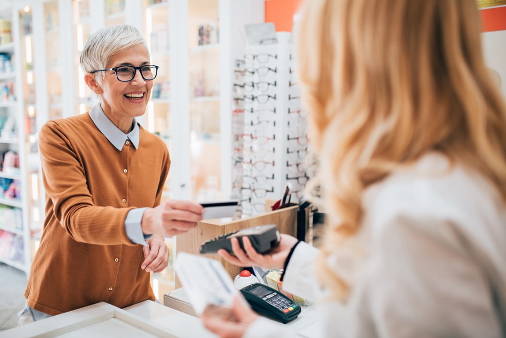 A woman stands in front of a store, holding a credit card, contemplating her purchase and the payment process involved.