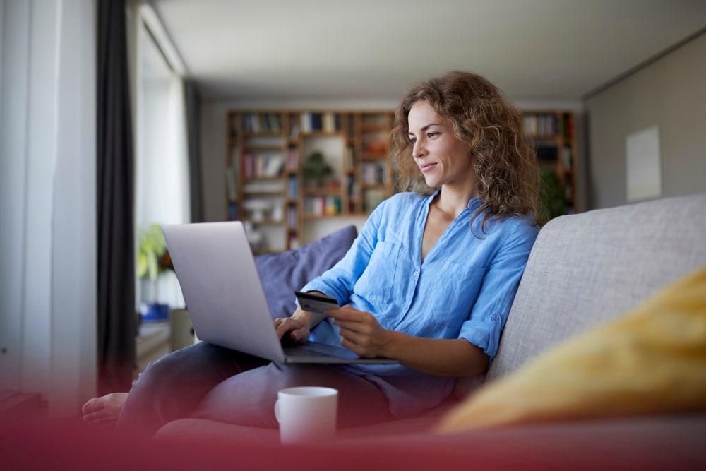 person sitting on the couch, holding a credit card with a laptop on the lap