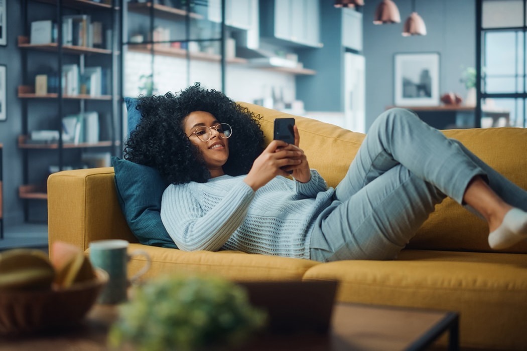 A woman lying on her couch while using her phone