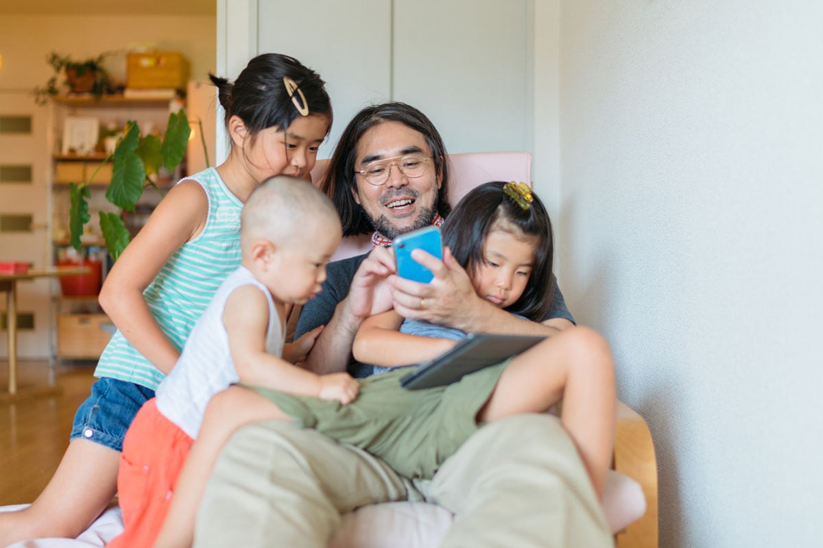 Father and three children are hanging out in the room looking at the cellphone screen