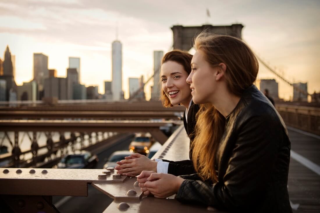 two women hanging out on Brooklyn Bridge at dusk