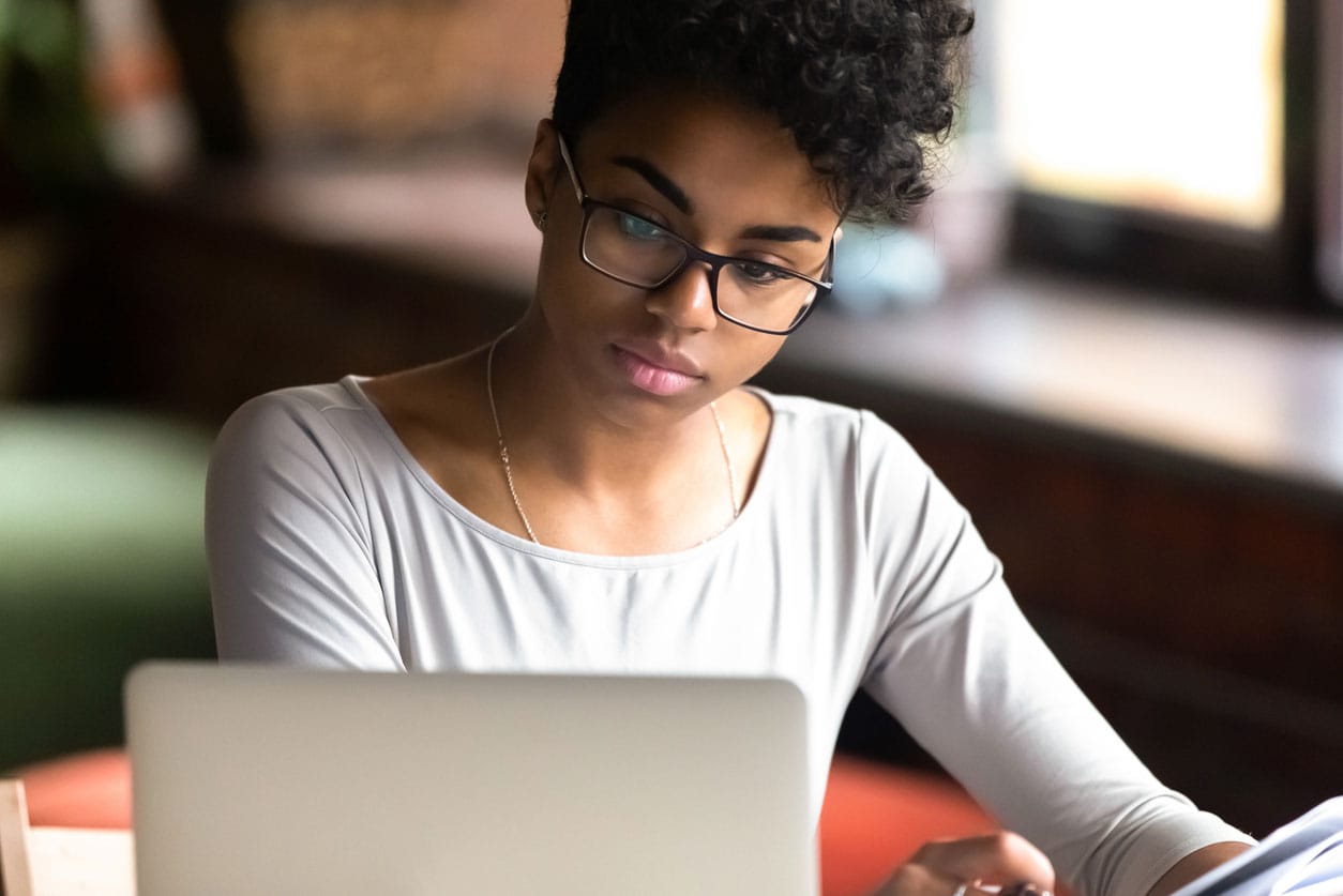 A young woman with glasses thoughtfully sits at a table, contemplating strategies to safeguard her credit score amid economic changes.