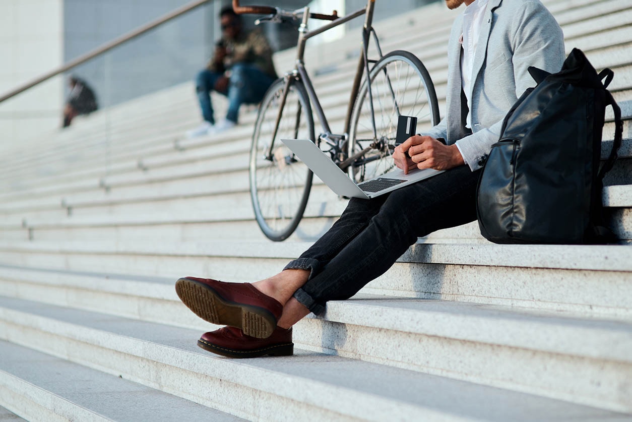 A person working on laptop sitting on stairs with the cycle parked beside them