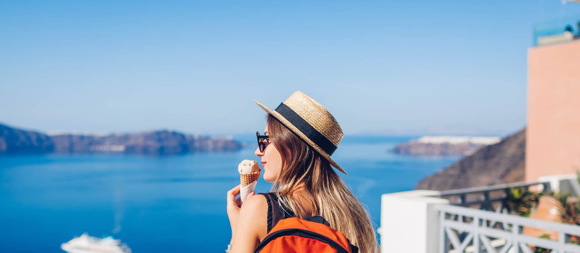 Woman is staying in front of the ocean, looking at the view while holding an ice cream cone
