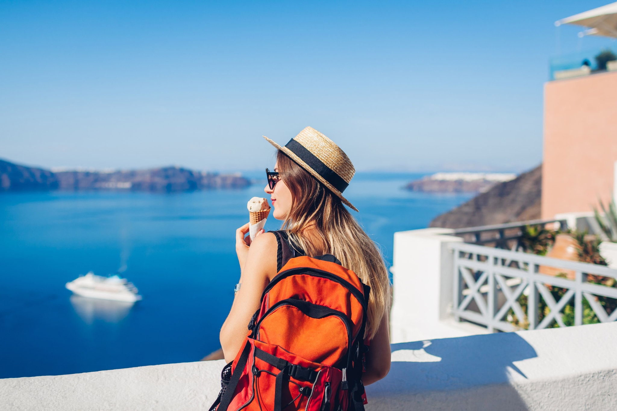 Woman is staying in front of the ocean, looking at the view while holding an ice cream cone
