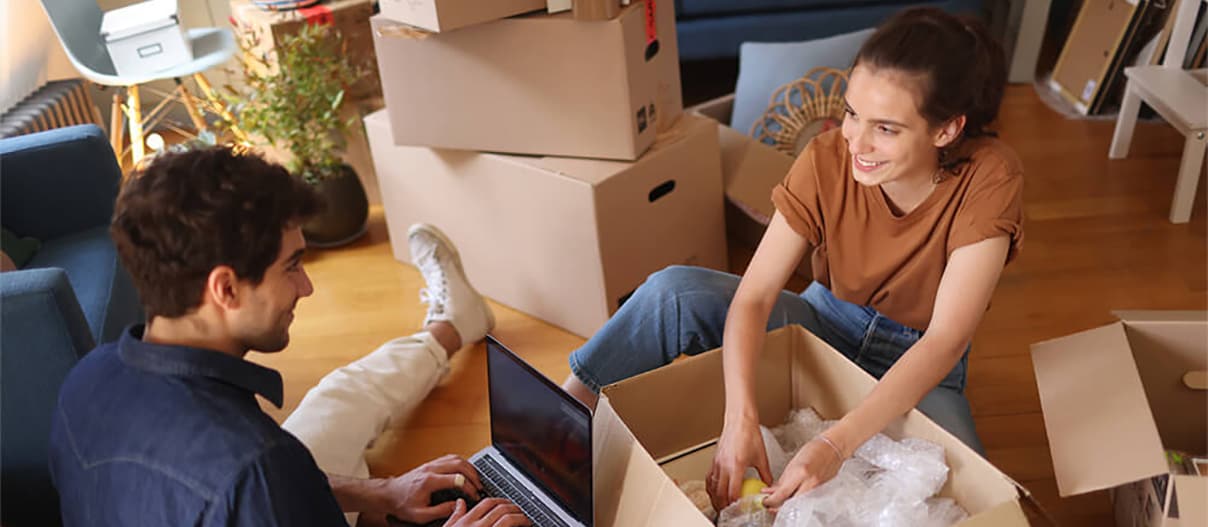 A man on laptop and a woman unpacking items from a box