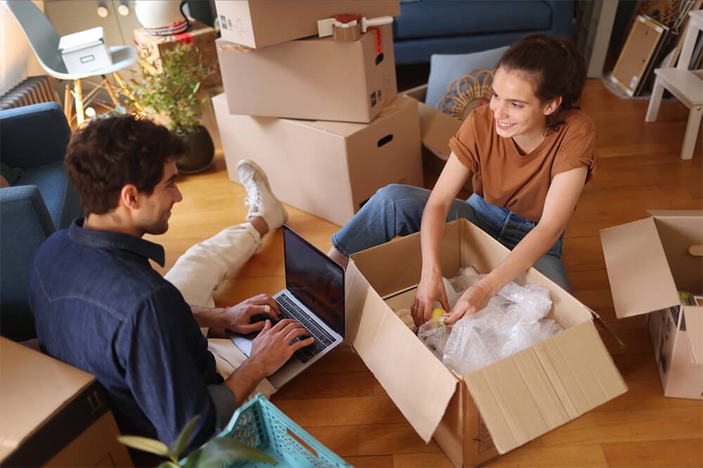 A man on laptop and a woman unpacking items from a box