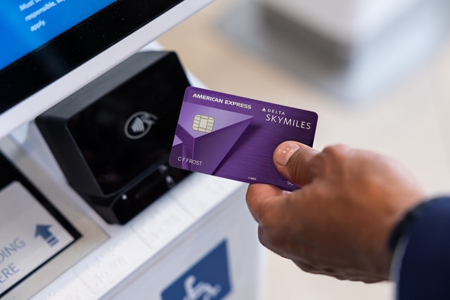 American Express Delta Skymiles Credit Card in a hand next to a wireless pay device
