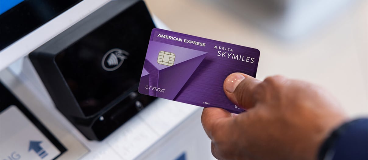 American Express Delta Skymiles Credit Card in a hand next to a wireless pay device