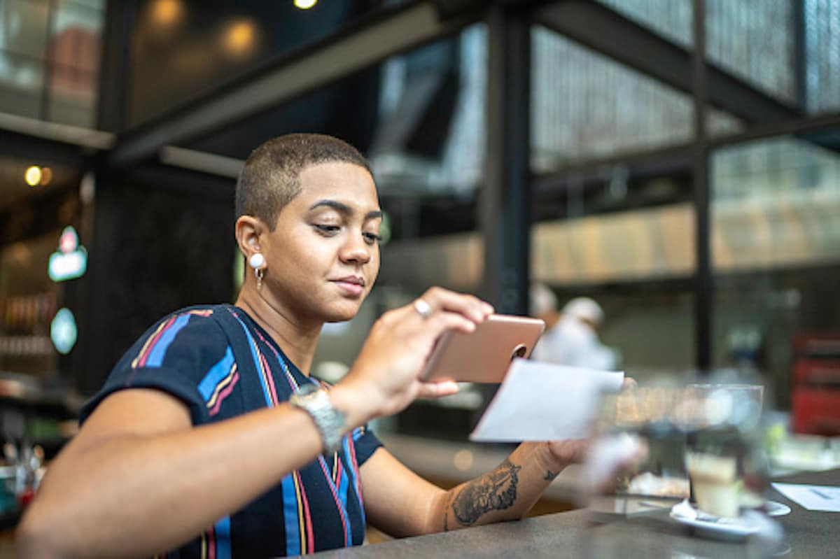 Woman is in the restaurant bar is taking a picture of a check with the cellphone