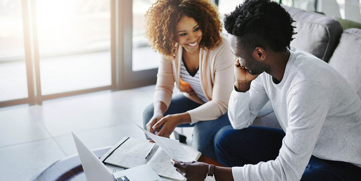 A person smiling and holding paperwork in the kitchen.
