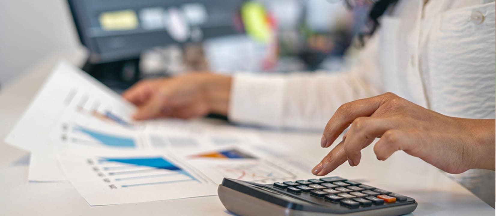 A person is using a calculator at a desk with a laptop
