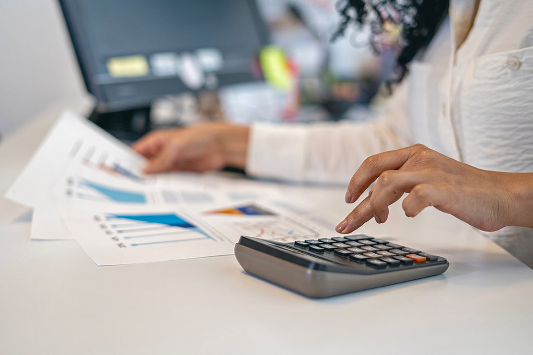 A person is using a calculator at a desk with a laptop