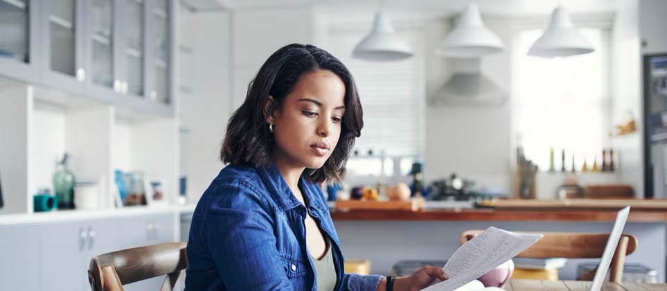 A woman using a laptop and noting equity mutual funds information using pen and paper.
