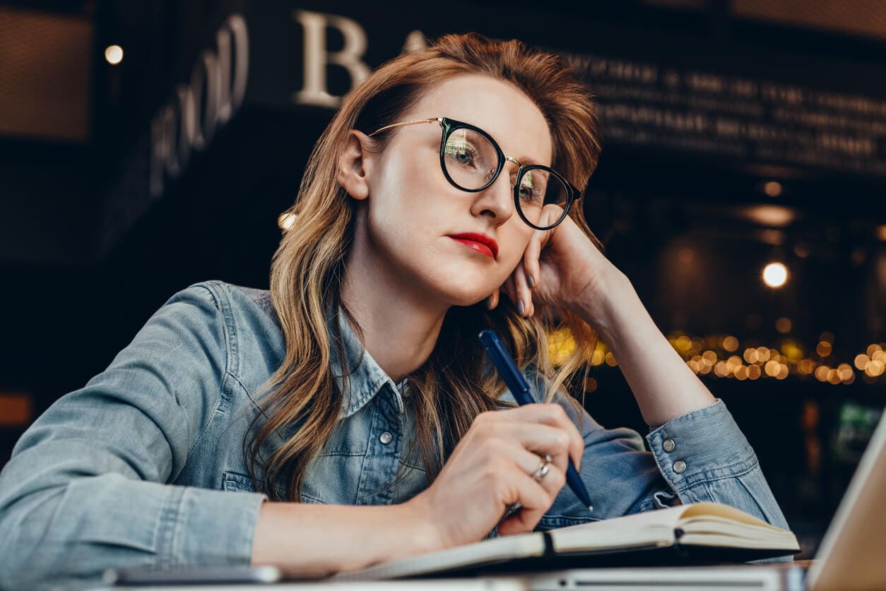 A woman in glasses and a denim shirt, thoughtfully reviewing tips for filing unemployment claims.