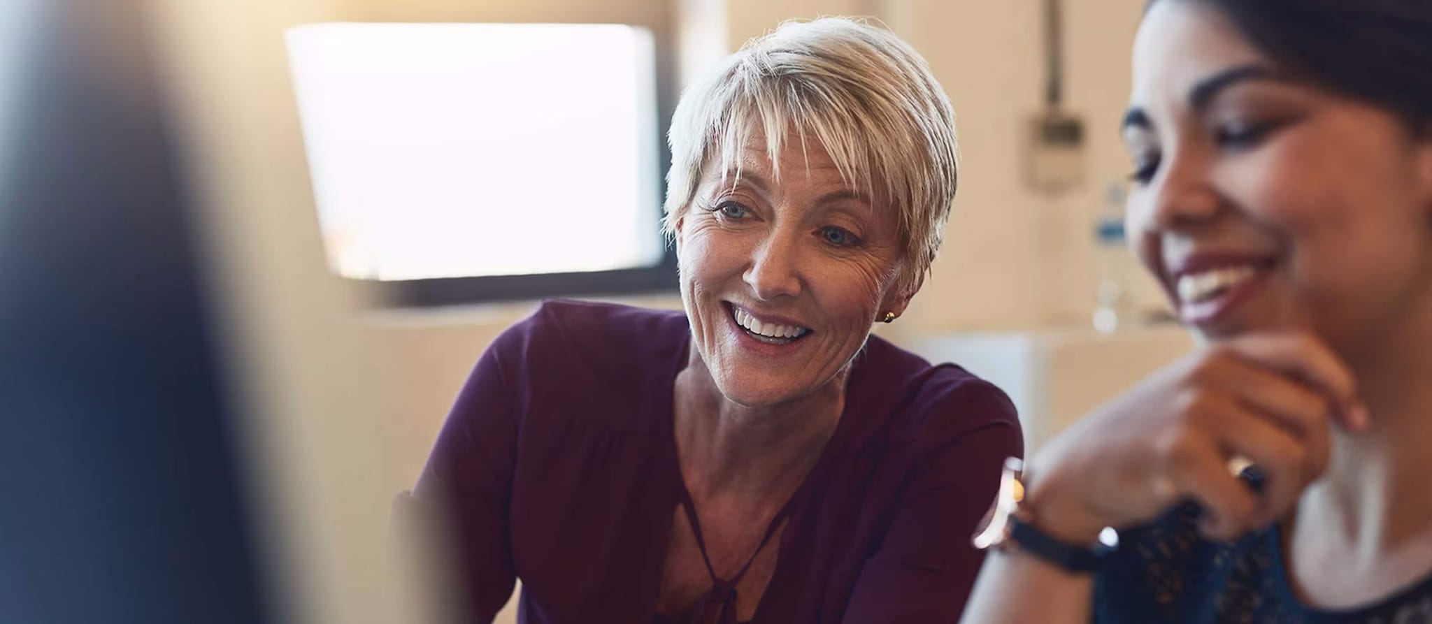 A woman smiles while seated beside another woman, symbolizing support in managing and protecting parents' finances.