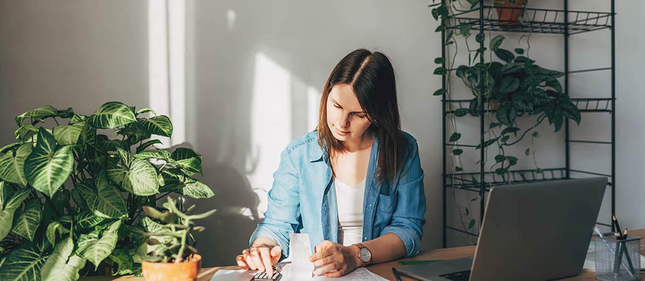 A woman sits at a desk with a laptop and notebook, contemplating fixed and variable expenses for financial planning.