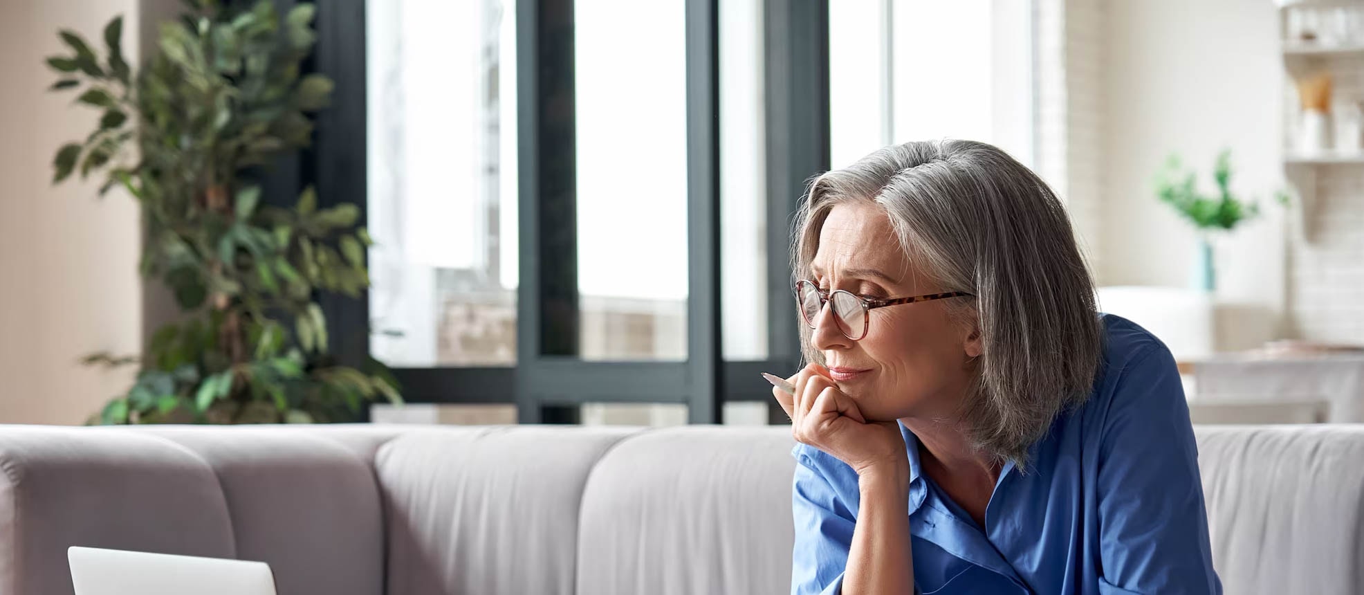 An older woman sits on a couch, using a laptop to check fraud alerts on her bank account for security updates.