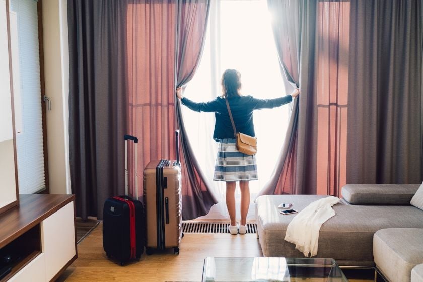 Woman looking out the window of a hotel room, holding the curtains open