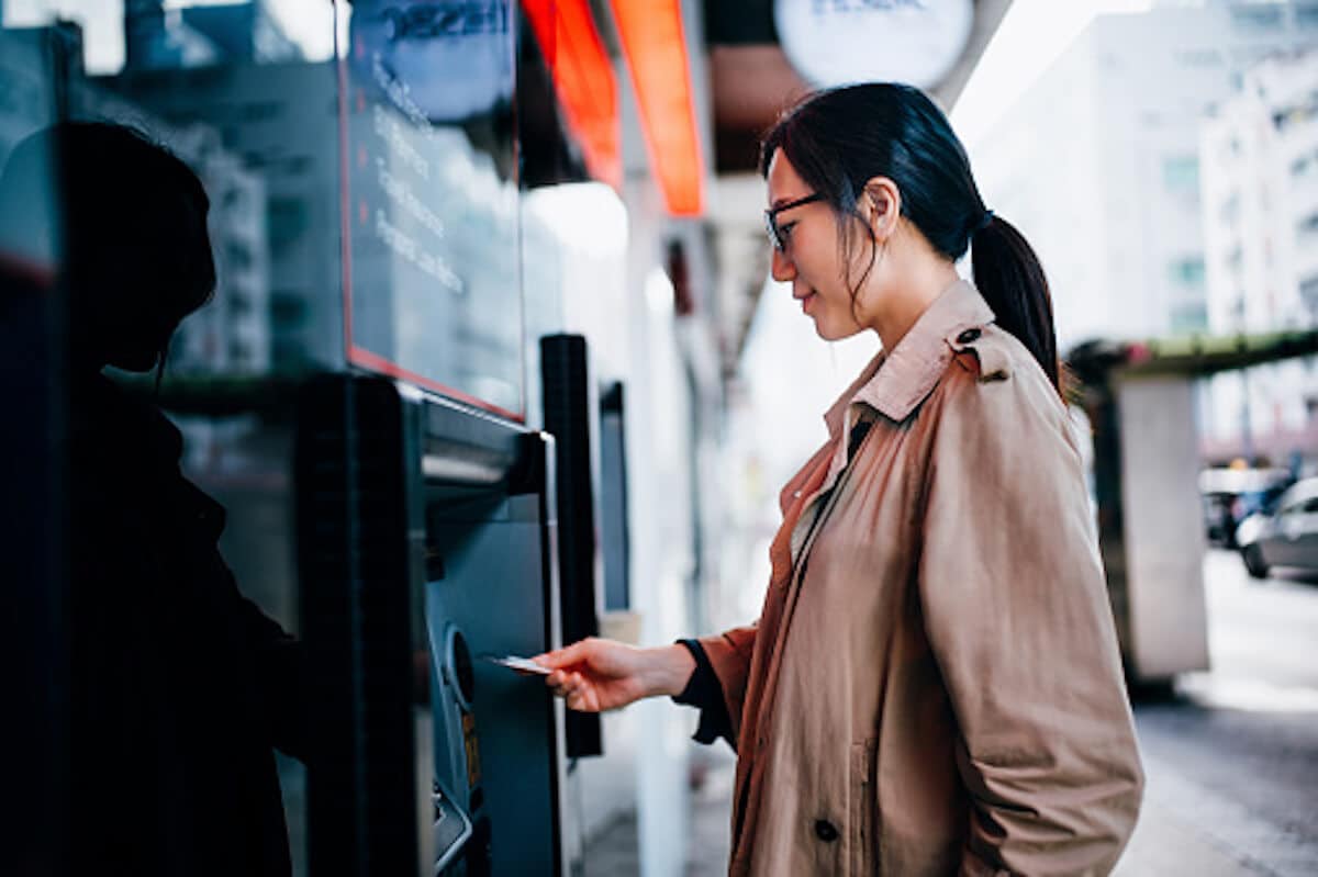 Woman is using ATM outside in the street in daytime.