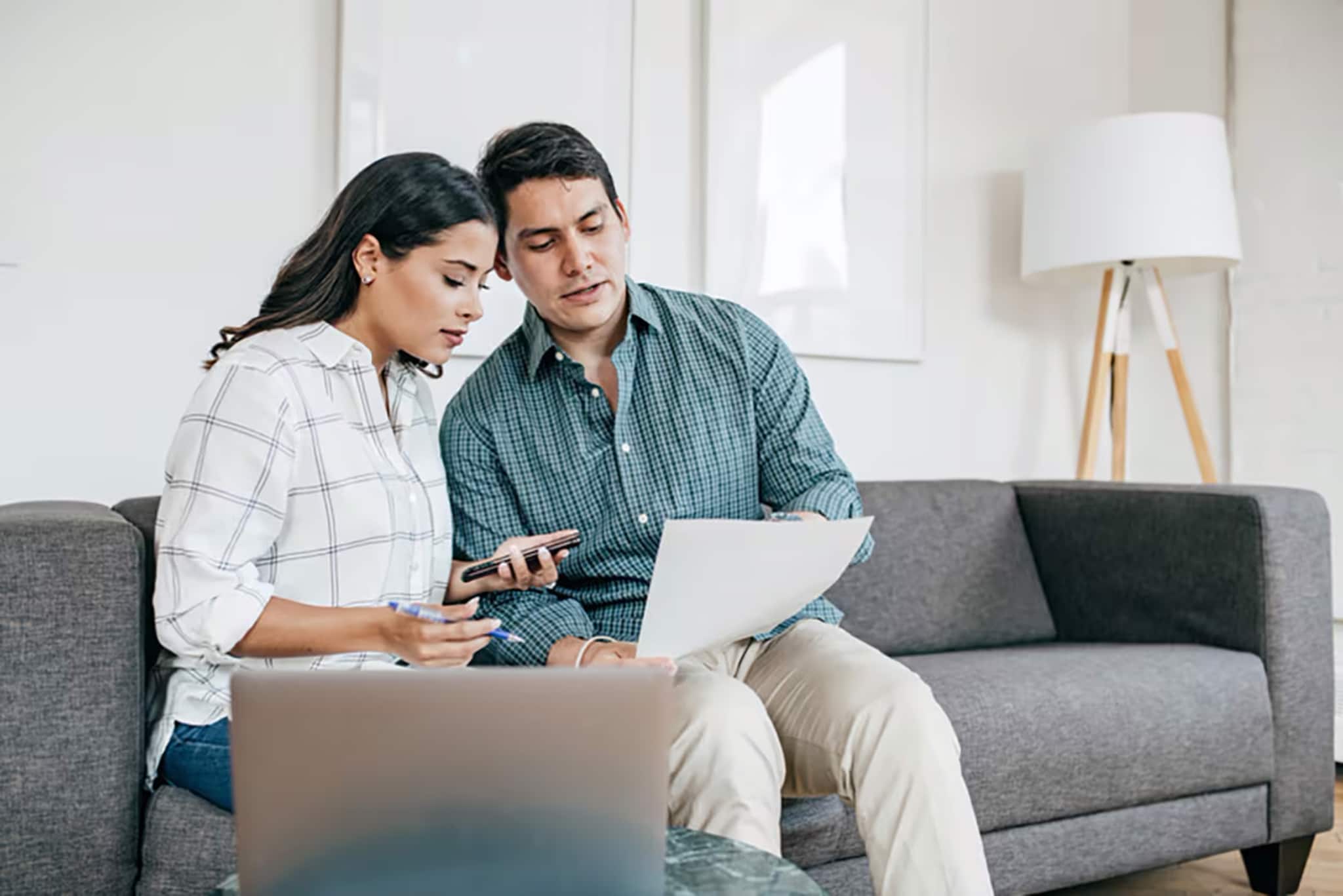 A couple reviews investment documents on a laptop, discussing growth versus value strategies for their financial future.