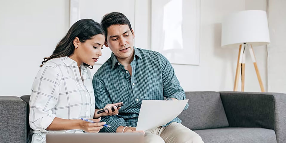 A couple reviews investment documents on a laptop, discussing growth versus value strategies for their financial future.