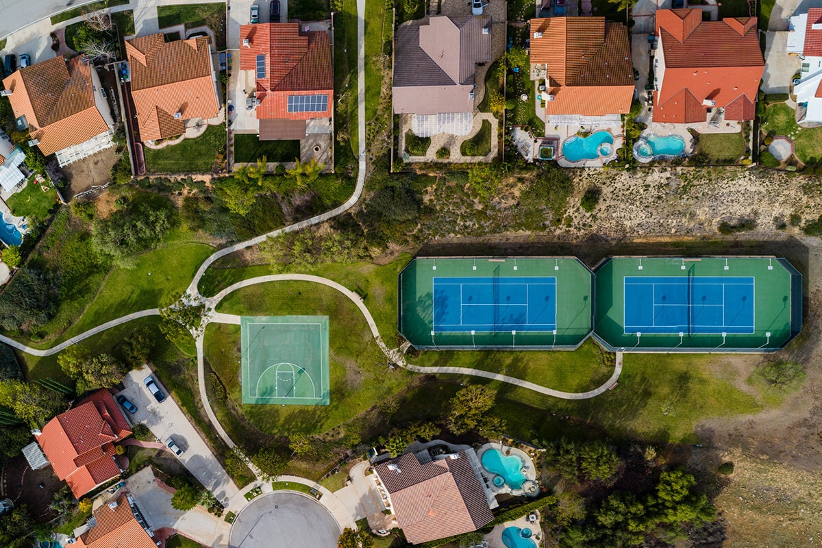 Aerial view of a residential neighborhood featuring tennis courts, highlighting community amenities and HOA fee considerations.