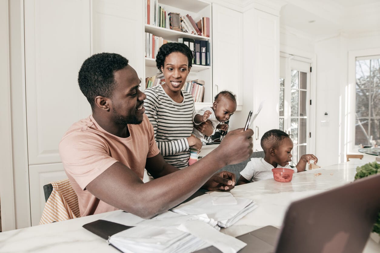 A family of 4 are hanging out in the kitchen and are looking through the receipts on the counter