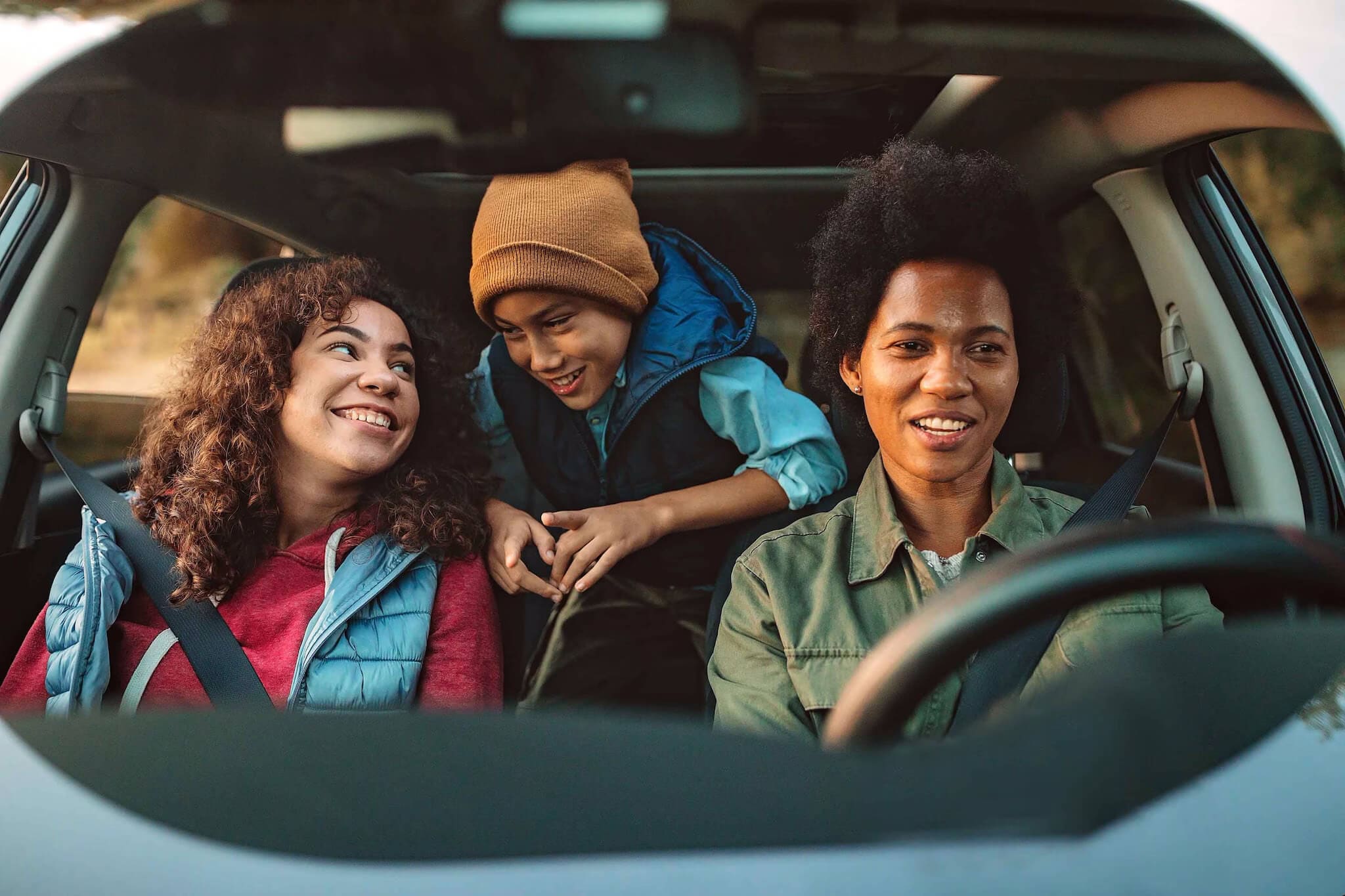 A family, consisting of a woman and her children, is inside a car, sharing a joyful moment.