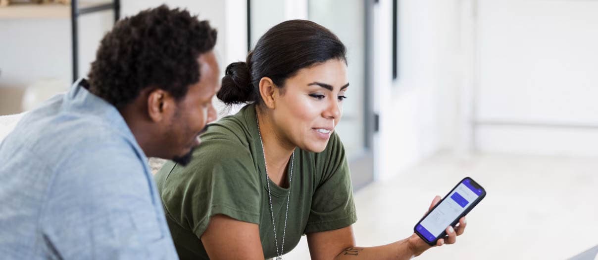 Two people sitting together, discussing something with smartphone and laptop.