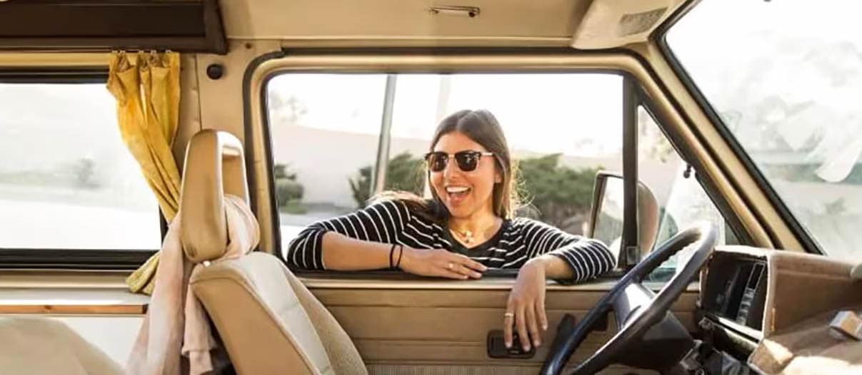 A woman smiles confidently in the driver's seat of a van, embodying the joy of leasing a vehicle and negotiating deals.