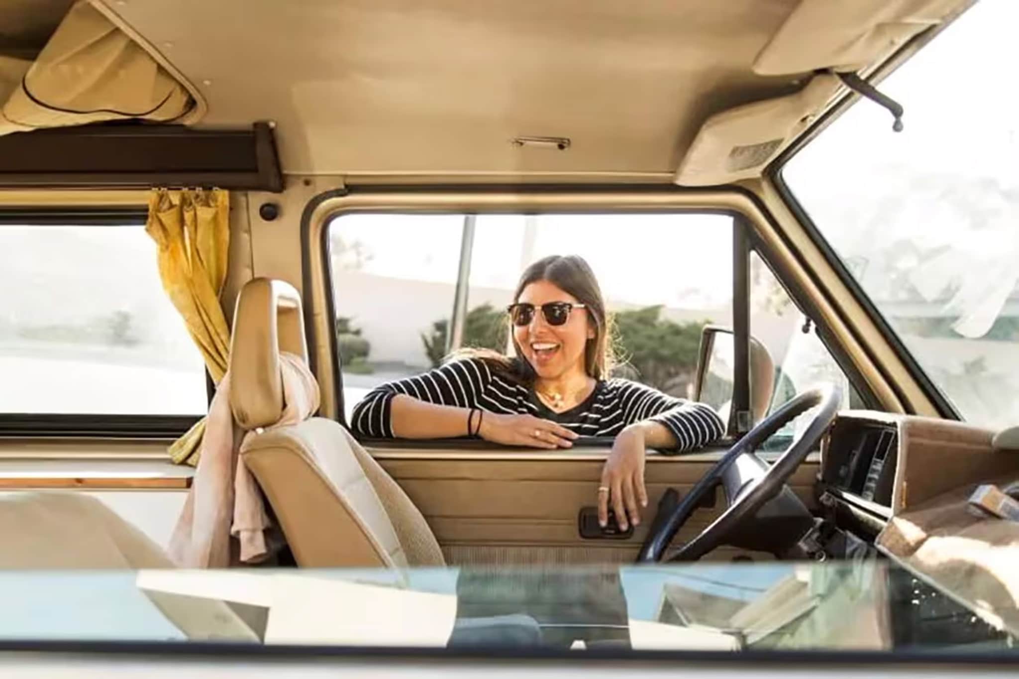 A woman smiles confidently in the driver's seat of a van, embodying the joy of leasing a vehicle and negotiating deals.