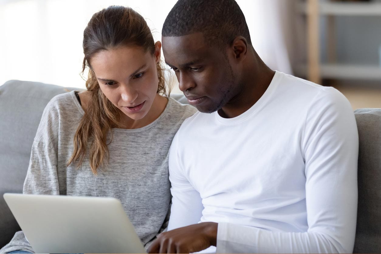 Couple is siting on a couch in a room and looking at a laptop