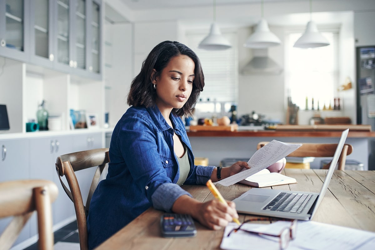 A professional image of a person organizing financial documents at a desk, with a laptop and a shredder nearby.