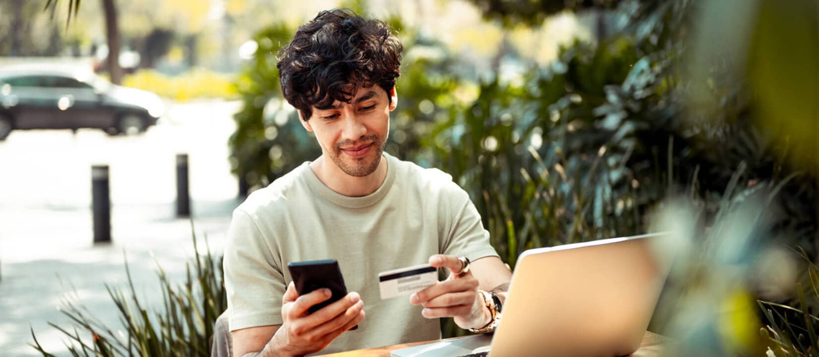 A man seated at a table, using his phone and a credit card, possibly researching how to dispute his credit report.