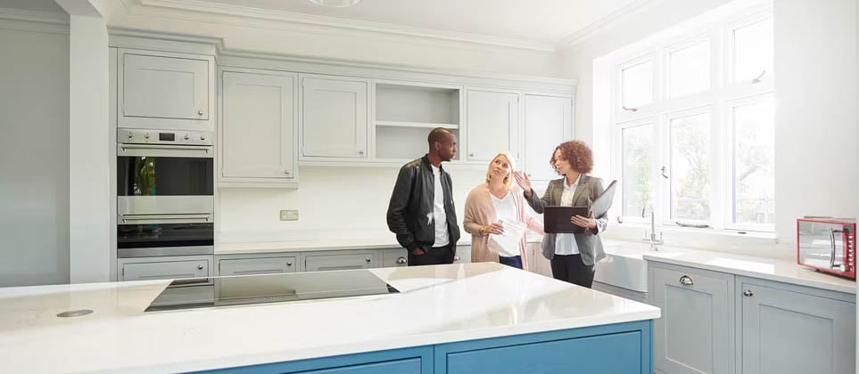 A real estate agent explaining modern kitchen features to a couple.
